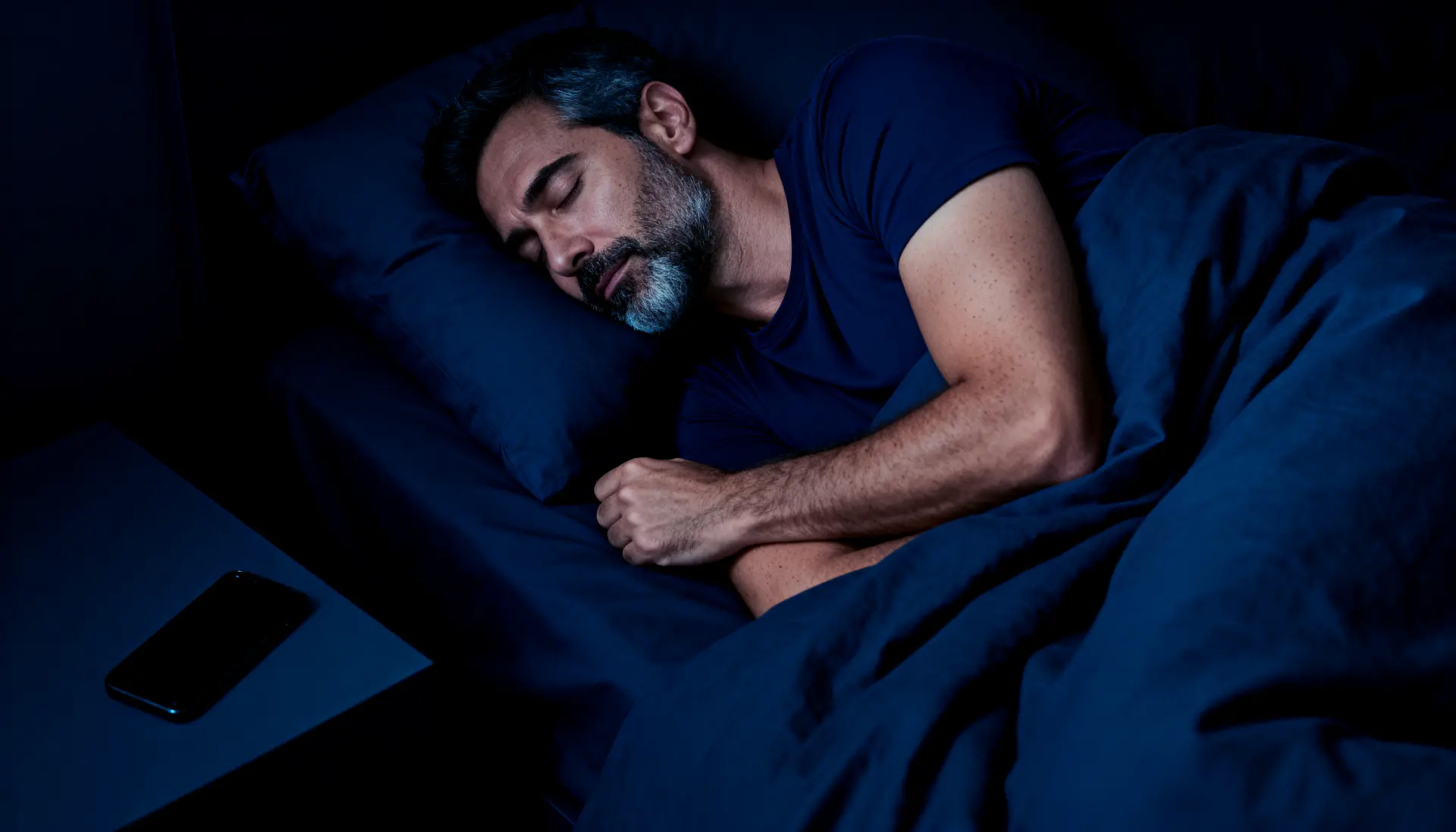 A man sleeping with his phone on the bedside table